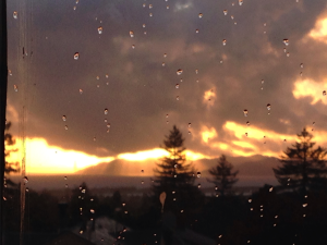 A photo of a cloudy, orange sunset through a rainy window.