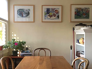 Photograph of a kitchen table with framed art behind it, a window to the left