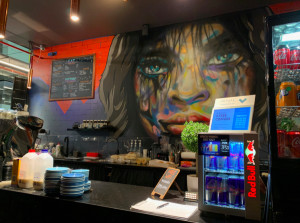 A coffee counter backed by a colorful mural portrait of a face