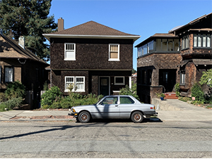 A gray 1980s BMW parked in front of a shingled house